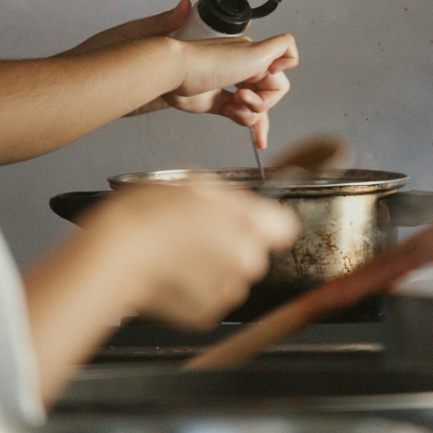 Hands seasoning food in a pot in a warm home kitchen
